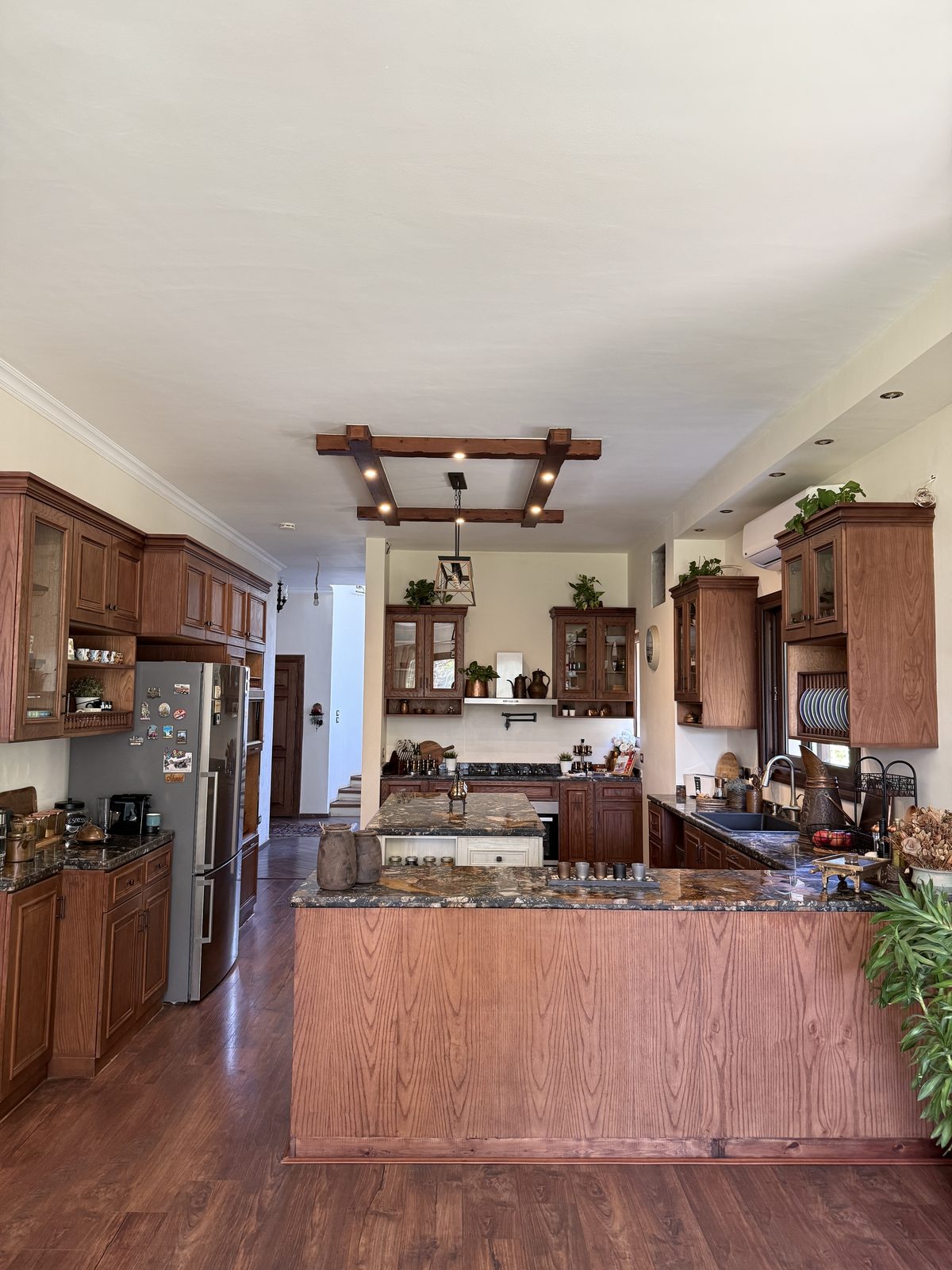 The first D’s kitchen — warm wood cabinetry and dark granite around a central island, beneath a beamed ceiling